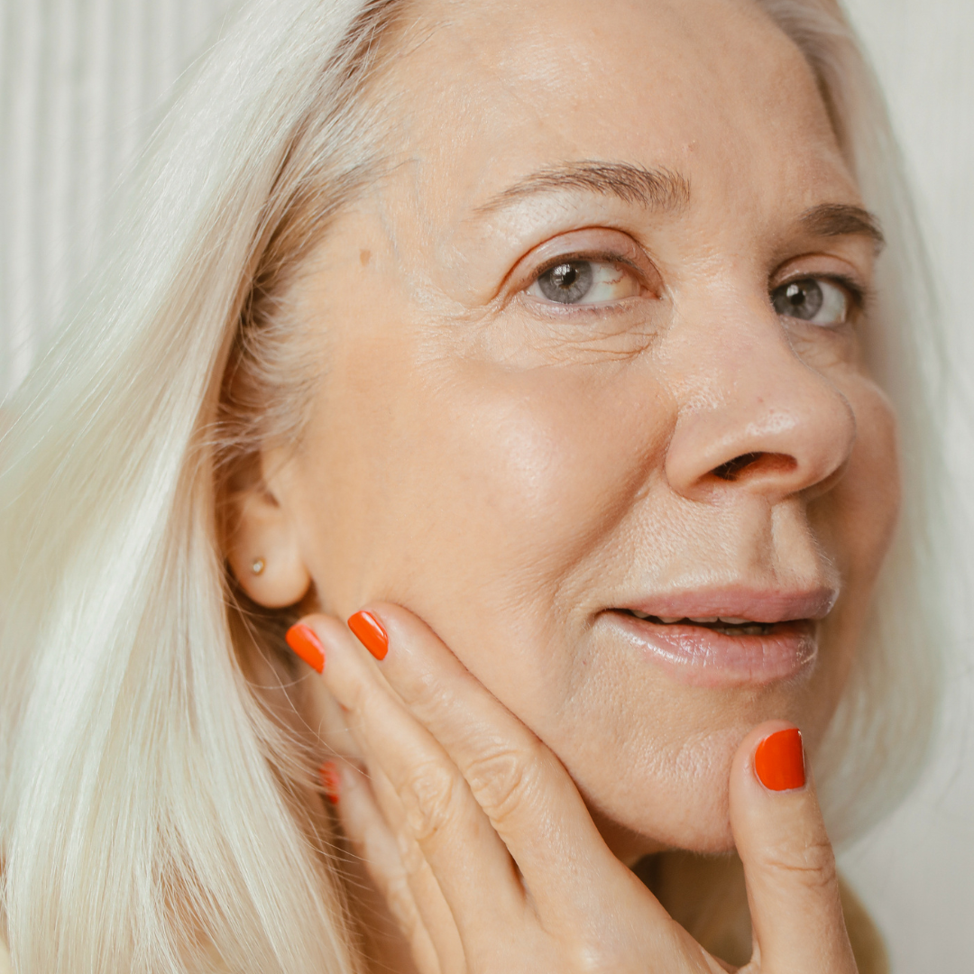 Middle-aged woman in her 50s gently touching her face, showcasing smooth skin after anti-ageing injectables.